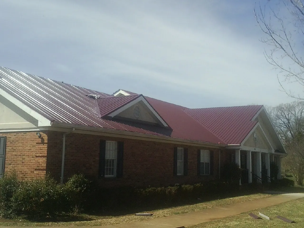 Red metal roof with gabled entries on a long brick building, from a Hail Damage Roof Repair job in Cache