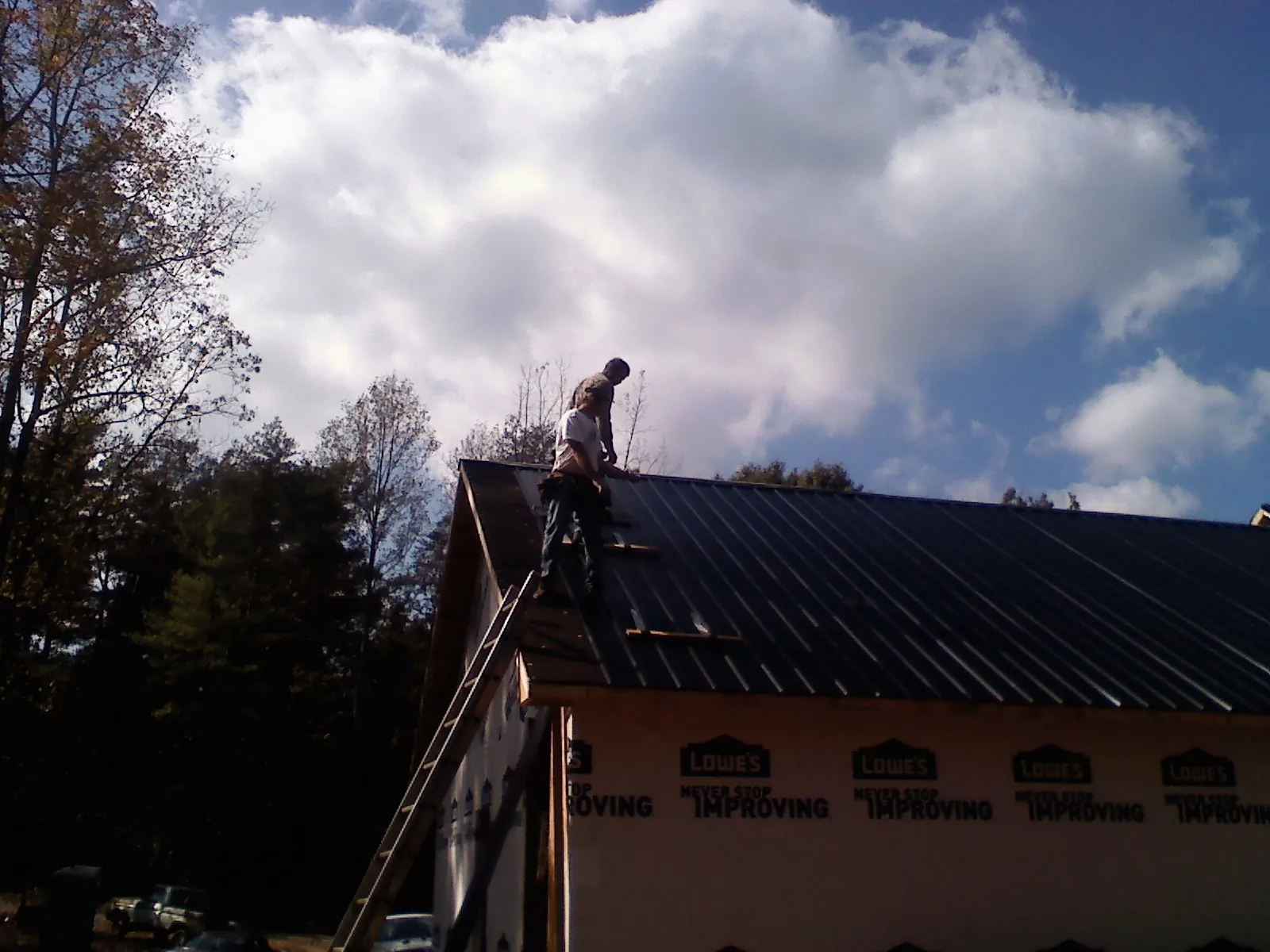 Roofer fastening dark metal panels high against a cloudy sky, from a Roof Inspection job in Cache